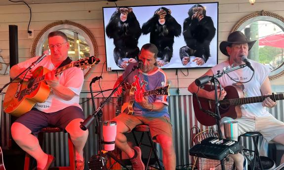 Three musicians performing, sitting on stools with guitars